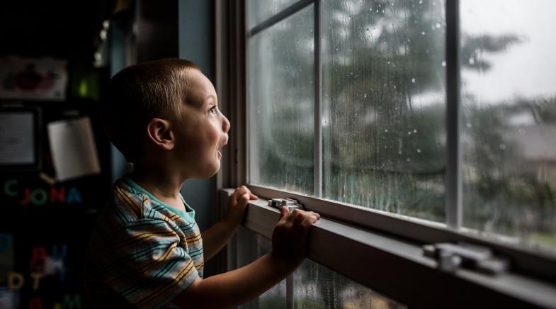 Junge steht am Fenster und schaut auf den Regen