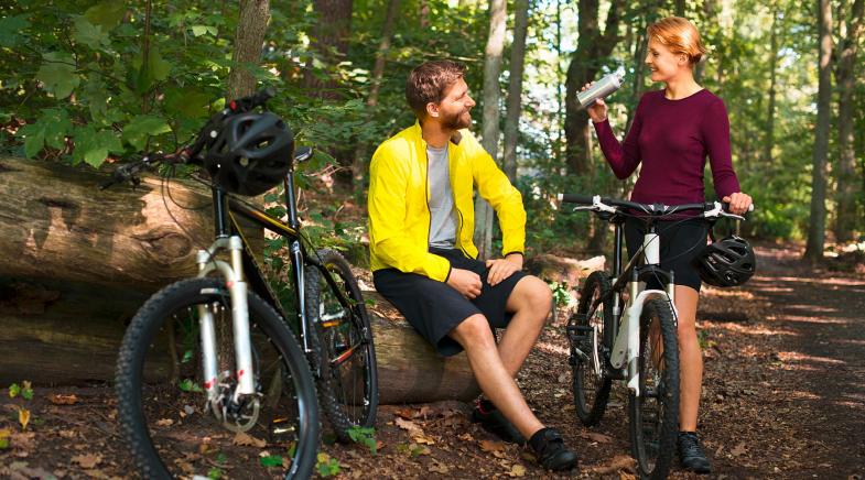Zwei junge Leute machen eine Trinkpause beim Fahrrad fahren im Wald