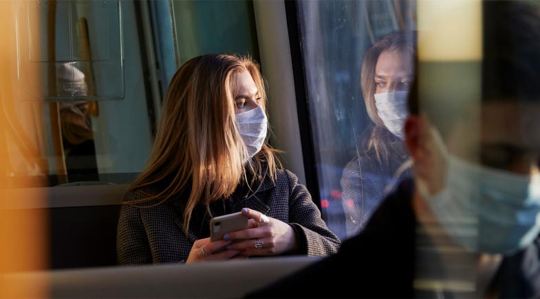 Frau sitzt mit Mundschutz im Bus