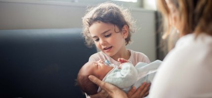 Kleines Mädchen sitzt im Krankenhaus und hält ein Baby im Arm