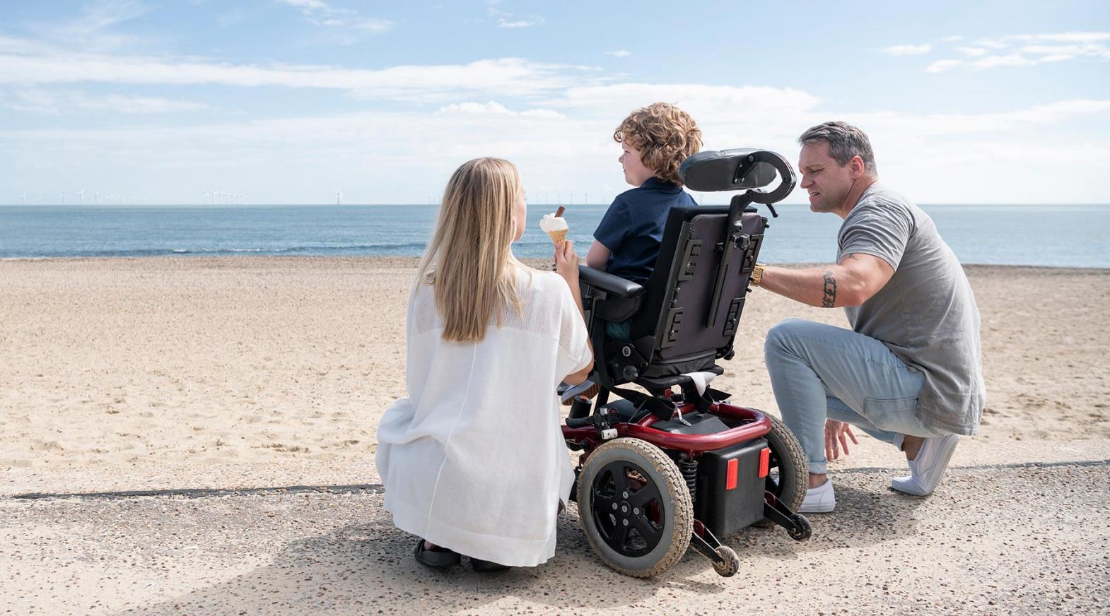 Eine Familie am Strand, das Kind sitzt im Rollstuhl. 