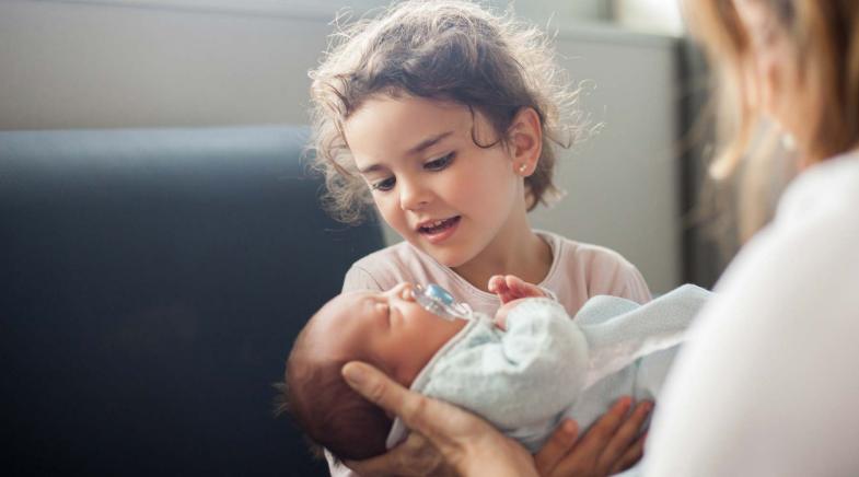 Kleines Mädchen sitzt im Krankenhaus und hält ein Baby im Arm